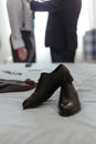 Wedding shoes on a bed of white linen, with men in a classic tuxedos in the background