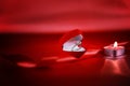 Wedding solitaire ring in heart shaped red box with candle and red ribbon on red background. Valentine`s day concept. Royalty Free Stock Photo