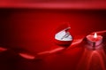 Wedding solitaire ring in heart shaped red box with candle and red ribbon on red background. Valentine`s day concept. Royalty Free Stock Photo