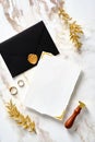 Wedding stationery mockup. Blank wedding invitation card with black envelope, wax seal stamp, golden rings, leaves on marble gold Royalty Free Stock Photo