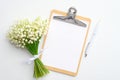 Wedding to do list concept. Clipboard with blank paper note, lily of the valley and pen on white background. Flat lay, top view Royalty Free Stock Photo
