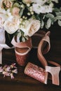 Wedding velvet pink shoes with shiny beautiful heels with gold wedding rings beside a bouquet of white roses, eucalyptus on a dark Royalty Free Stock Photo