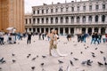 Wedding in Venice, Italy. Bride and groom are looking at camera among the pigeons in Piazza San Marco, against backdrop