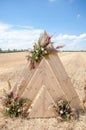 Wedding wooden arch decorated with a detailed flower arrangement in a golden, mown field under blue summer sky. Rustic style Royalty Free Stock Photo