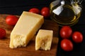 Wedge of italian hard cheese Parmesan or Grana Padano on a brown wood cutting boad, small red tomatoes and olive oil over black