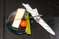 Wedge of soft cheese, four asparagus, one tomato, a cheese cutter, on blue, glass plate with napkin and holder