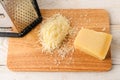 Wedge of traditional italian hard cheese Grana Padano or Parmesan, grated cheese and stainless steel kitchen grater on a wood