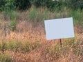 Weed-covered field with white blank metallic sign. Mock-up for sale announcement with copy space Royalty Free Stock Photo