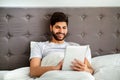 Weekend leisure concept. Relaxed arab man using digital tablet, sitting in bed and surfing internet online Royalty Free Stock Photo