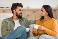 Weekend morning. Happy indian couple enjoying hot coffee and talking while sitting on sofa indoors Royalty Free Stock Photo