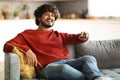 Weekend Pastime. Cheerful Indian Guy Watching Tv At Home, Holding Remote Controller