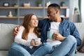 Weekend Pastime. Happy Mixed Couple Relaxing On Couch With Coffee At Home