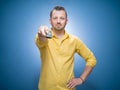 Weekend time. Man holding remote control and watching TV - movies over blue background, dresses in yellow shirt. Front view of guy Royalty Free Stock Photo