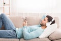 Young Man In Headphones Using Mobile Phone Lying On Sofa Royalty Free Stock Photo