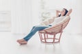 Weekends finally! Relaxed brunette girl is sitting on modern chair near the window in light cozy room at home. She is enjoying pe Royalty Free Stock Photo