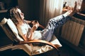 Weekends finally. Woman in blue jeans relaxing with cup of tea in armchair at home, daydreaming. Girl enjoying life, bright sunlig