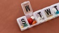 A weekly medicine dispenser opened for Monday, prescription pills and vitamins in a white pill box on terracotta