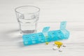 Weekly pill box with medicaments and glass of water on white wooden table Royalty Free Stock Photo