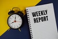 Weekly Report text written on notepad with alarm clock on blue background Royalty Free Stock Photo