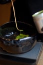 Weighing green powder matcha tea in dark ceramic bowl on scales, macro closeup