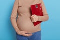 Weight gain during pregnancy, pregnant woman holding scale, faceless future mommy against blue background touching her belly, Royalty Free Stock Photo