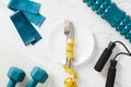 Weight loss concept. Cutlery wrapped measure tape on plate, jump rope, dumbbells, elastic band, roller on marble table Royalty Free Stock Photo