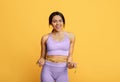 Weight loss concept. Excited african american woman measuring her waist with tape over yellow studio background Royalty Free Stock Photo