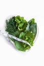 Weight loss diet. Fresh green leaf lettuce, spinach, sorrel, dill and measuring tape on heart shaped plate on white background. Royalty Free Stock Photo
