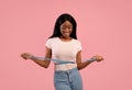 Weight loss and healthy lifestyle concept. Slim black woman measuring her waist with tape over pink studio background Royalty Free Stock Photo