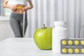 Weight loss pills with apple on table and woman measuring waist indoors. Royalty Free Stock Photo