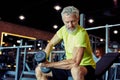 Weight workout. Focused mature man in sportswear lifting heavy dumbbells and pumping his biceps while training at gym