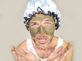 Weird looking man with shower cap and cream on his face horrified seeing himself ugly on bathroom mirror applying facial mask male Royalty Free Stock Photo