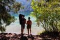 Weissensee - Family with baby carrier with scenic view of east bank of alpine lake Weissensee, Gailtal Alps