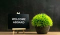 WELCOME ABOARD wrote on chalkboard with green plant in pot