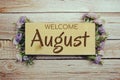 Welcome August text on wooden board with flowers frame on wooden background