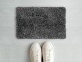 Welcome dark grey doormat with white sneaker shoes on white background