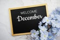 Welcome December text on wooden blackboard and flower decoration on marble background