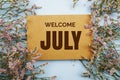 Welcome July written on paper card with flower frame decoraton on pink background