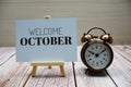 Welcome October text with alarm clock on wooden background