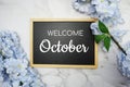 Welcome October text on wooden blackboard and flower decoration on marble background