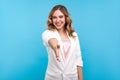 Welcome! Portrait of friendly hospitable cheerful woman giving hand to handshake, hostess greeting guest. blue background