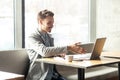 Welcome! Portrait of satisfied happy young man in grey blazer are sitting in cafe and greeting a worker through a webcam and Royalty Free Stock Photo