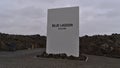 Welcome sign at the entrance of tourist resort Blue Lagoon with black colored volcanic rocks on cloudy winter day.