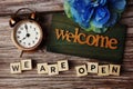 Welcome Sign with we are open and alarm clock on wooden background Royalty Free Stock Photo