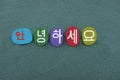 Welcome text in Korean language with a composition of handmade colored stone letters over green sand