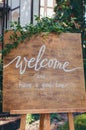 Welcome To Our Celebration. Handwritten Calligraphy Text Sign Board On Wooden Panel In The Garden With Tree Twig