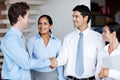 Welcome to the team. Two businessmen sealing the deal with a handshake while their colleagues look on happily.