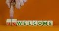 Welcome or unwelcome symbol. Businessman turns wooden cubes and changes the word unwelcome to welcome. Beautiful orange table,