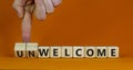 Welcome or unwelcome symbol. Businessman turns wooden cubes and changes the word unwelcome to welcome. Beautiful orange table,