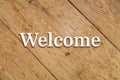 `Welcome` white text on a wooden background. 